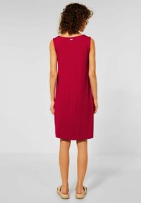 Rotes, ärmelloses Kleid mit glatter Textur, knielang, mit Rundhalsausschnitt und kleiner Rückenöffnung. Kombiniert mit beigen Riemchensandalen.