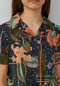 Kurzarmhemd mit einem dunkelblauen Grundton, das lebendige Blumen- und Blattmuster in Orange, Grün und Blau aufweist, mit einem Kragen.
