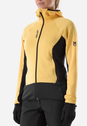 Person wearing a yellow and black zip-up jacket with hood, black gloves, and black pants, shown from mid-chest to hips.