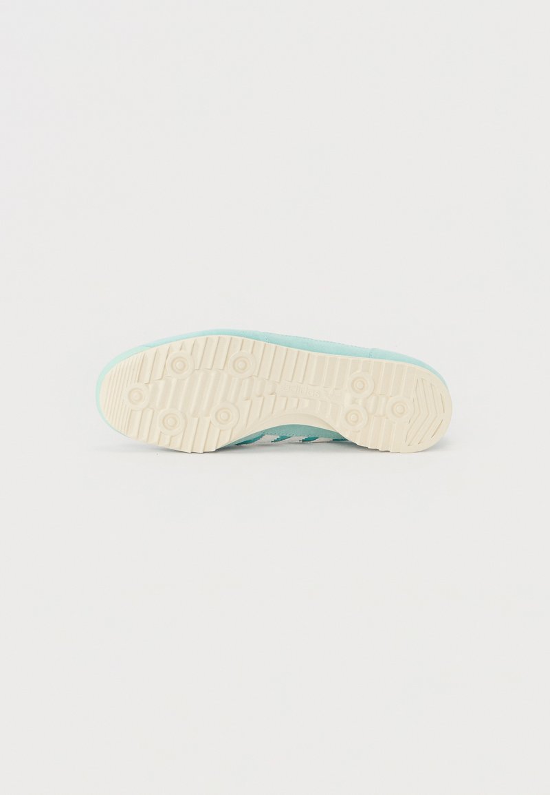 Zapatilla deportiva azul claro con un upper texturizado, suela de goma beige y un patrón de pisada. Presenta tres franjas blancas a lo largo del costado.