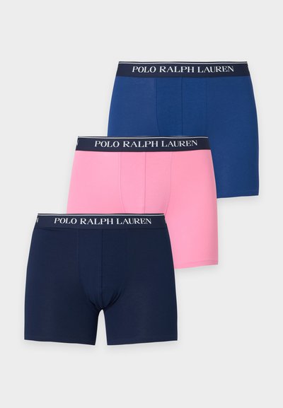 Τρία ανδρικά εσώρουχα Polo Ralph Lauren σε ναυτικό μπλε, ροζ και μπλε με ελαστικές μέσης με λογότυπο, στοιβαγμένα σε λευκό φόντο.