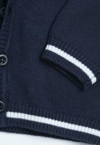 Gilet en tricot bleu marine avec des boutons noirs et des détails en rayures blanches au niveau des poignets et de l'ourlet.