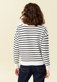 Jersey a rayas con franjas horizontales en blanco y negro, puños y dobladillo acanalados, tejido suave, combinado con jeans azul oscuro con costuras de acento.