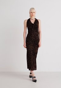 Halter neck obleka z leopardjim vzorcem iz mehkega črnega in rjavega blaga; oprijet kroj z dolgo krilom. V kombinaciji s črnimi čevlji s koničastim nosom.