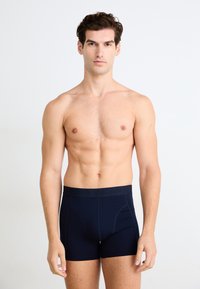 Mørkeblå boksershorts med glatt stoff, har en svart midjebånd med preget logo, tettsittende design og kort benlengde.