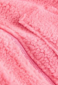 Flis tkanina v živo rožnati barvi, s teksturirano površino in puhastim videzom. Ob enem robu poteka ročajen zadrga v isti rožnati barvi.