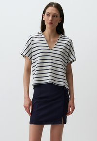 Top a maglia a righe con scollatura a V, caratterizzato da righe orizzontali blu navy e crema. Abbinato a una gonna blu navy con uno spacco laterale.