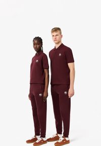 Burgundy pikétröjor och matchande byxor, med broderade Lacoste-logotyper. Bärs med bruna sneakers. Slät, bomullsmaterial.