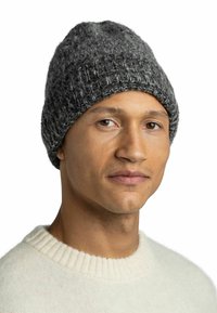 Knitted gray beanie with a textured surface and ribbed band. Worn by a person, complementing a light-colored sweater.