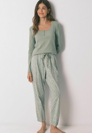 Hellgrünes Langarmshirt mit Rundhalsausschnitt und Knopfdetails, kombiniert mit gemusterten, weit geschnittenen Pyjamahosen mit floralem Design.
