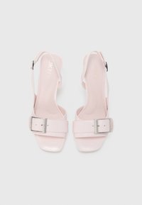 Pár svetloružových otvorených sandál s otvorenou špičkou, striebornými prackami, remienkami na zadnej strane chodidla a nízkymi podpätkami na bielom pozadí.