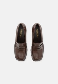 Mocassins en cuir marron à finition lisse, bout carré et coutures décoratives. Semelle en caoutchouc noire pour l'adhérence. Logo doré à l'intérieur.