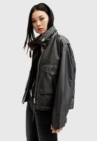 Black leather jacket with a high collar, zip closure, front pockets, and a relaxed fit. Smooth texture with a glossy finish.