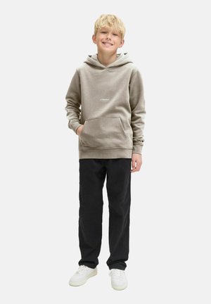 Beżowa bluza z kapturem z kieszenią kangurzą i białym logo, w połączeniu z czarnymi spodniami i białymi sneakersami, stojąca na tle białym.