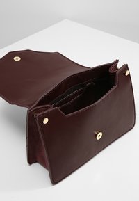 Vinrød lædertaske med en glat tekstur, udstyret med magnetlukning og to indvendige rum, designet med guldfarvet beslag.