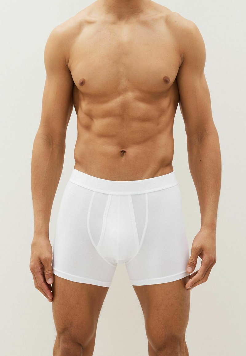 Weiße Baumwoll-Boxershorts mit glatter Textur, die einen engen Sitz, einen breiten Bund und ein klassisches Design ohne Muster aufweisen.
