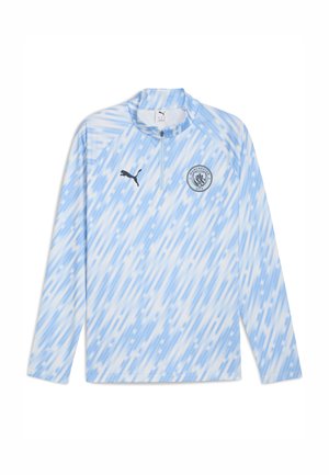 Gaiši zils garām piedurknēm krekls ar pusi rāvējslēdzēju, abstraktu diagonālu rakstu, Puma logo un Mančestras City ģerboni uz krūšu.