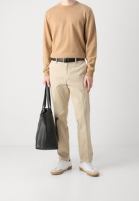 Maglione beige, pantaloni beige, cintura nera, borsa in pelle nera e sneakers bianche con suole in gomma. Outfit semplice e casual con colori neutri.