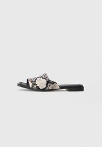 Offene Zehen-Slidesandalen mit einem schwarz-weißen Schlangenhautmuster, flacher schwarzer Sohle und minimalistischem Design. Glatte Textur, synthetische Materialien.