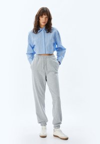 Afgesneden, lichtblauwe gestreepte shirt met een kraag; grijze trainingsbroek met elastische boorden; witte sneakers met beige accenten.