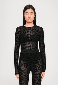 Juodas tinklelis bodis su ilgomis rankovėmis, kuris turi pakartotinį raštą su užrašais "Versace" ir "Couture" skirtingais dydžiais. Aukšti liemenė.