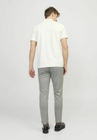Polo shirt crema a maniche corte abbinato a pantaloni grigi slim-fit con texture e scarpe nere. Nessun logo o motivo visibile.