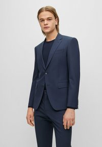Giacca da abito blu navy con rever a punta, chiusura con un solo bottone e due tasche frontali. Abbinata a una maglietta a girocollo blu navy. Texture liscia.
