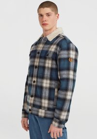 Plaid shirt jacket in blue, green, and cream with a faux fur collar, button front, and patch pockets. Textured fabric with a checkered pattern.