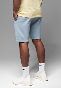 Shorts en coton bleu clair avec poches latérales, associés à des baskets blanches et des chaussettes côtelées. Design simple avec une coupe décontractée.