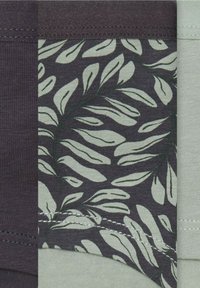 Wzorzysta tkanina z zielonymi liśćmi na ciemnoszarym tle, z kontrastującymi jasnoszarymi sekcjami i widocznymi detalami ściegów.