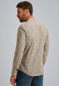Braun gemustertes Langarmhemd mit Kragen, aus strukturiertem Stoff, mit geknöpften Manschetten und abgerundetem Saum. Getragen mit blauen Denim-Jeans.