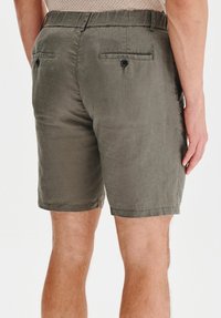 Oliwkowe szorty wykonane z tkaniny o fakturze, z dwoma tylnymi kieszeniami zapinanymi na guziki oraz luźnym krojem. Lekko przeszyty dół.