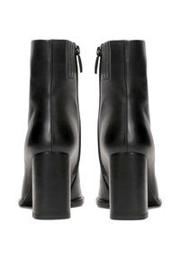 Par de botas de cuero negro hasta el tobillo con tacones cuadrados y cremalleras laterales, vistas desde la parte trasera sobre un fondo blanco.