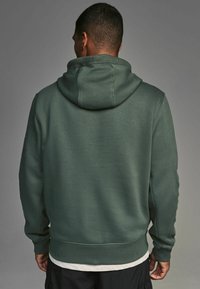 Sudadera con capucha en verde oscuro. Está hecha de una tela suave, presenta un corte relajado, puños y dobladillo acanalados. La capucha está unida con un acabado sin costuras.