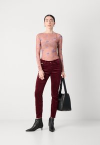 Šviesiai rožinė, ilgo rankovės permatoma palaidinė su mėlynomis gėlėmis, derinama su tamsiai raudonomis keterinėmis kelnėmis. Modelis laiko juodą rankinę ir dėvi juodus aulinukus.