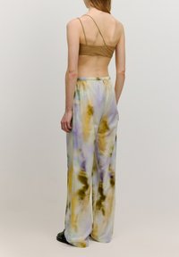 Losse, lichte broek met een tie-dye patroon in pastelkleuren van geel, paars en wit, met een elastische tailleband.