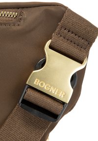 Detail van een bruine stoffen tas met een gouden gesp waarop "BOGNER" is gegraveerd, aangevuld met een textuur strap voor duurzaamheid.