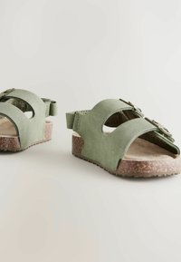 Gröna mockasandaler med öppen tå och två breda remmar, med en strukturerad brun korksula och justerbar hälrem.