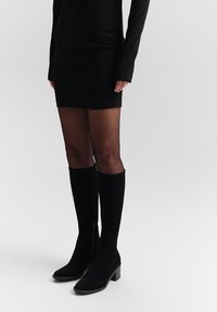 Czarne kozaki sięgające do kolan o gładkiej fakturze, kwadratowym nosku i słupkowym obcasie. Posiadają boczny zamek błyskawiczny i dopasowanie wokół łydki.