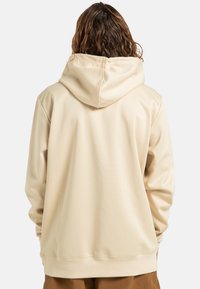Beżowa bluza z kapturem o gładkiej, miękkiej teksturze. Posiada duży kaptur, długie rękawy i ściągacze na końcach rękawów. Prosty design bez widocznych logo.