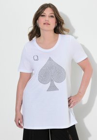 Camiseta blanca de manga corta con cuello redondo, que presenta un gran diseño de trébol de strass negro en el frente y un pequeño logo en la esquina superior izquierda.
