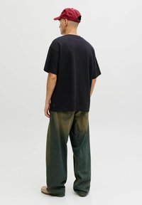 Črna prevelika majica iz mehke tkanine, združena z širokimi džins hlačami z zelenim gradientom in zadnjimi žepi.