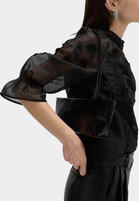 Czarna torebka z eko skóry o płaskim, prostokątnym kształcie, z gładkim wykończeniem i prostym paskiem na ramię. Widoczne teksturowane detale na powierzchni.