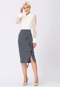 Blouse en dentelle blanche à manches longues, associée à une jupe crayon bleu à motifs pied-de-coq avec un drapé et une fente sur le côté. Talons hauts beiges.