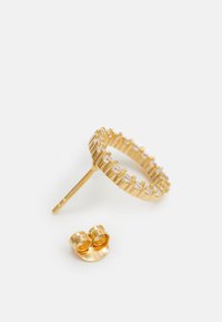 Guldring med en rad av klara stenar längs banden, åtföljs av en liten matchande öronkrok. Båda har en polerad finish.