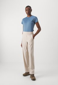 Top azzurro chiaro a maniche corte abbinato a pantaloni a gamba larga color crema e scarpe da trekking marroni; presenta un tessuto morbido e due tasche laterali.