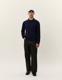 Jūras spēku tumši zils garām piedurknēm polo krekls ar apkakli, apvienots ar tumšiem džinsa taisnām biksēm un melniem apaviem, papildināts ar baltu beisbola cepuri.