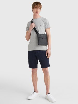 Gray short-sleeve t-shirt, navy shorts, and white sneakers. A black crossbody bag with zipper and logo worn over the shoulder.