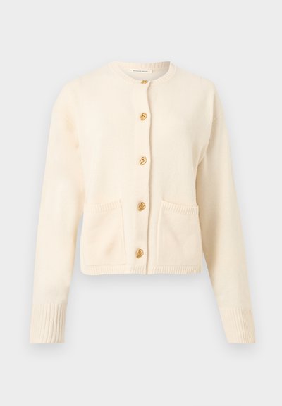 Κρεμ πλεκτή ζακέτα με μακριά μανίκια, στρογγυλή λαιμόκοψη, δύο μπροστινές τσέπες και πέντε διακοσμητικά χρυσά κουμπιά κατά μήκος του κέντρου.