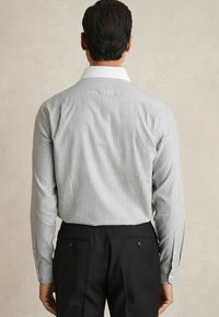 Cămașă subțire cu dungi gri și alb, cu guler alb, mâneci lungi și manșete cu nasturi, asortată cu pantaloni negri taiati.